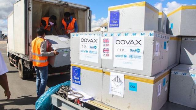 Boxes of Covax deliveries being unloaded by men in high-vis jackets