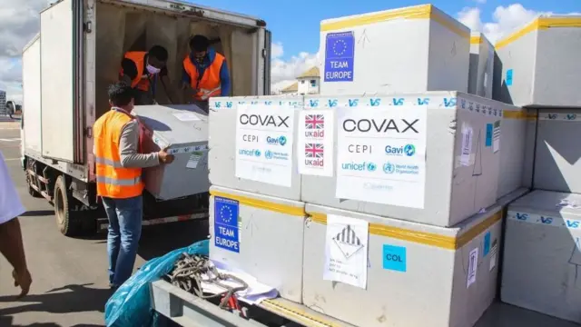 Des hommes portant des gilets de sécurité déchargent des cartons de livraisons de Covax.