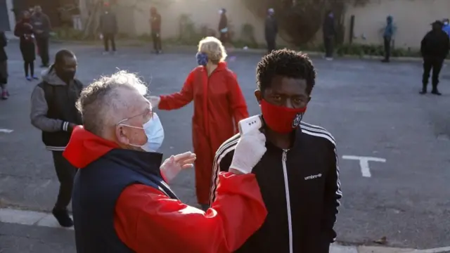 اندازه‌گیری دمای بدن کسانی که برای گرفتن غذا در صف ایستاده‌اند در ژوهانسبورگ پایتخت آفریقای جنوبی