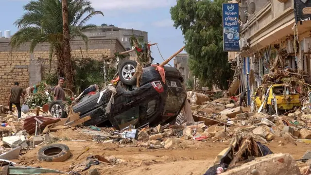 A man stands next to a damaged car, after a powerful storm and heavy rainfall hit Libya, in Derna, Libya, on 12 September 2023