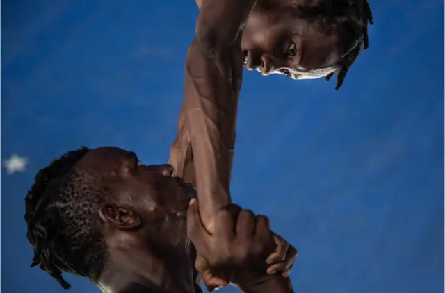Un acrobate en soutient un autre dans une position soulevée.