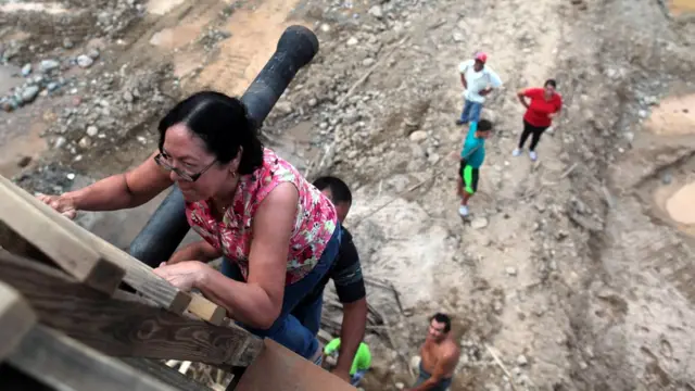Una señora sube por una escalera improvisada con tablas de madera.