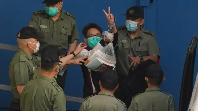 被鎖上手銬的陳皓桓在獄警押送下向九龍荔枝角收押所外記者舉起勝利手勢(28/5/2021)