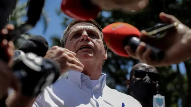 Bolsonaro fala, rodeado por microfones e sob céu azul