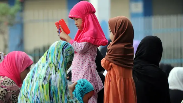A Muslim girl is on the phone while her family sit around her