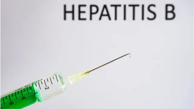 Di foto illustration show disposable syringe with hypodermic needle, dem write HEPATITIS B on a white board behind.