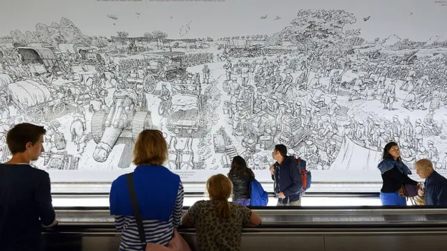 Personas en una estación de metro de París ven un mural sobre la batalla del Somme dibujado por Joe Sacco.