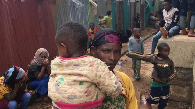 ከተፈናቃዮቹ መካከል መካከል የሆነች አንዲት እናት ልጇን እንዳዘለች በወረዳ 11 ወጣት ማዕከል ውስጥ ተጠልላለች