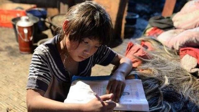 在雲南省怒江州福貢縣木克基村，一名孩子趴在牀上做作業，她的家裏沒有桌子。
