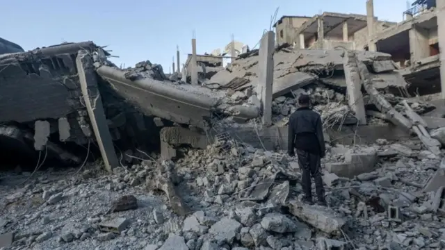 Вайрон бўлган Нусайрат қочқинлар жамлоғи бинолари олдида турган эркак