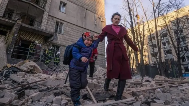A woman with a child evacuates from a residential building damaged by shelling, as Russia"s attack on Ukraine continues, in Kyiv, Ukraine, in this handout picture released March 16, 2022.