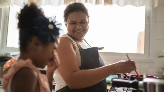 Mulher cozinha e conversa com criança, sorrindo