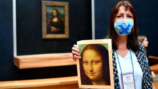 Mulher segurando um cartaz da Mona Lisasacar bonus galera betfrente ao quadro no Museu do Louvre