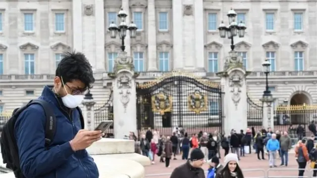 ผู้ชายใส่หน้ากากยืนหน้าพระราชวังบักกิงแฮม