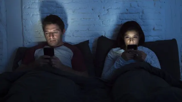 Man and woman in bed looking at smartphones.