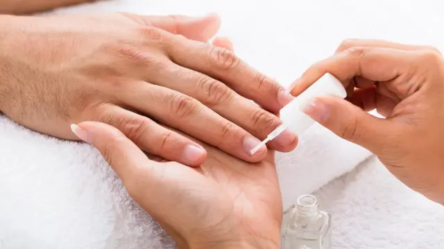 Mujer practicando manicura a hombre.