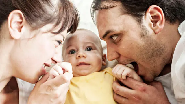 ছোটো শিশুকে বাবা-মা আদর করে চুমু খাচ্ছে ও কামড়ে দিচ্ছে