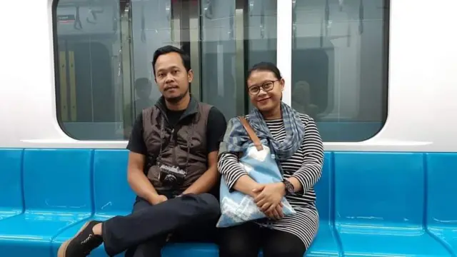 Foto keluarga yang terdiri dari ibu di tengah, ayah di sebelah kanan, dan anak kecil perempuan di sebelah kiri.