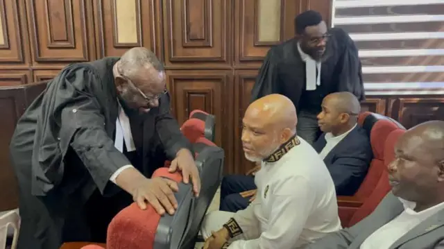 Nnamdi Kanu n'ọdụrụ n'che n'ụlọikpe ebe onye okaiwu ya Ejiofor na-agwa ya okwu tupu amalite ikpe ya. Kanu yi efe ọcha si n'aka Fendi ebe ọkaiwu ya Ifeanyi Ejiofor