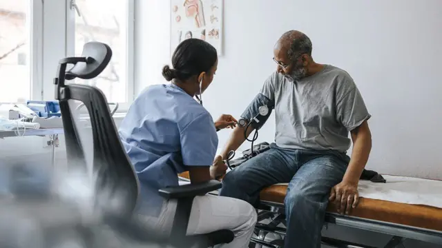 Profissional de assistência médica mede a pressão arterial de paciente sentado em uma maca hospitalar
