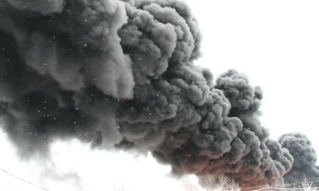 Щільний темно-сірий дим здіймається у похмуре небо.