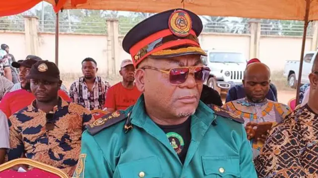 Celestine Anere yi uwe ndị ọrụ Ocha Brigade nọrọ n'okpuru ihe mkpuchi anwụ n'emume a na-eme.