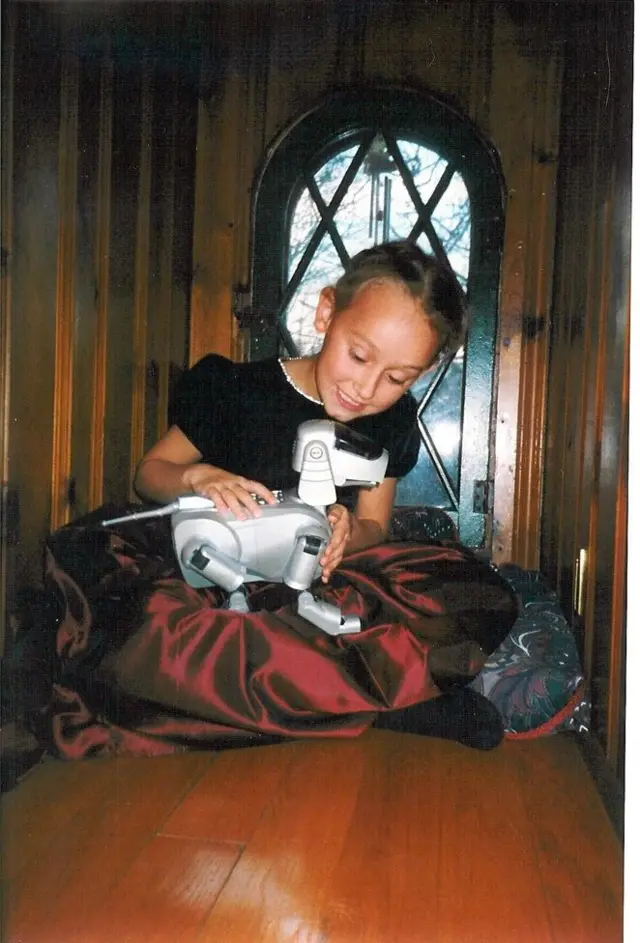 Sabrina González Pasterski vestida con un traje negro y rojo jugando en el piso de madre con un perrito de juguete