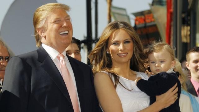 Trump ao ladoslotsenMelania, que segura bebê no colo; o casal sorri