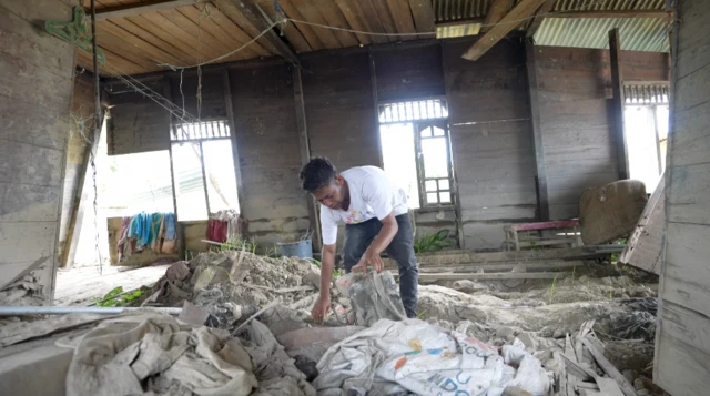 Basriadi membersihkan lumpur di dalam rumahnya yang terseret belasan meter akibat banjir November tahun lalu.
