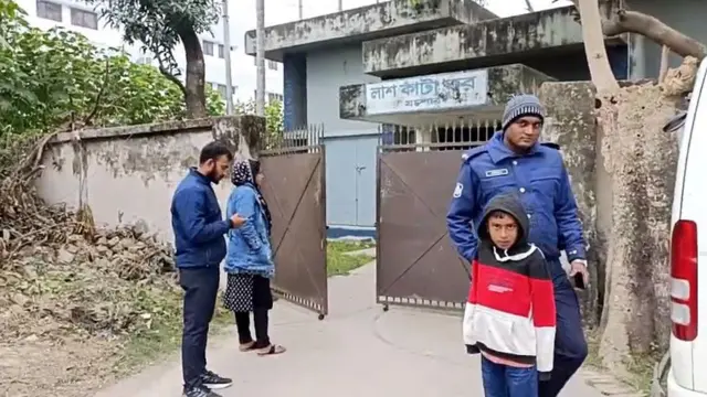 মর্গের সামনে পুলিশ ও কয়েকজন দাঁড়িয়ে আছেন।