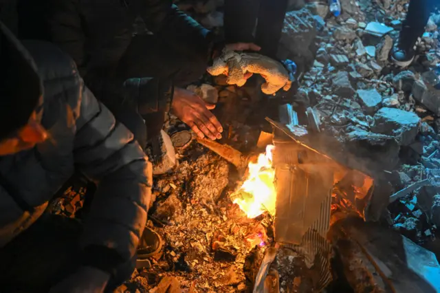 Адыяман шаарында куткаруу операциясына катышкан кишилер от жагып, жылынып жатышат. Кыштын суугу куткаруу ишинбир топ татаалдаштырды