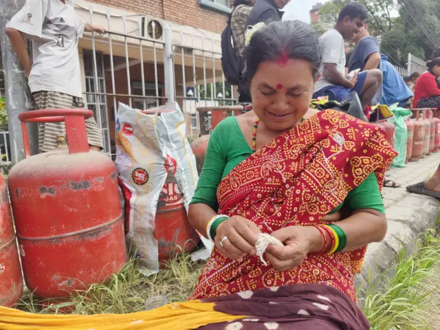 ग्यासको पालो कुर्दै बसिरहेकी महिला बत्ती कात्दै