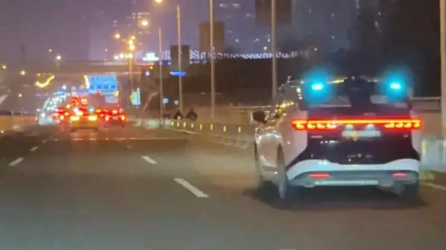 Вид на дорогу вночі, посеред якої зупинився біло-чорний автомобіль - рух транспорту продовжується далі дорогою