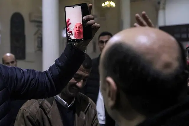 Un hombre sostiene frente al Padre Gabriel un celular con la imagen del Papa Francisco