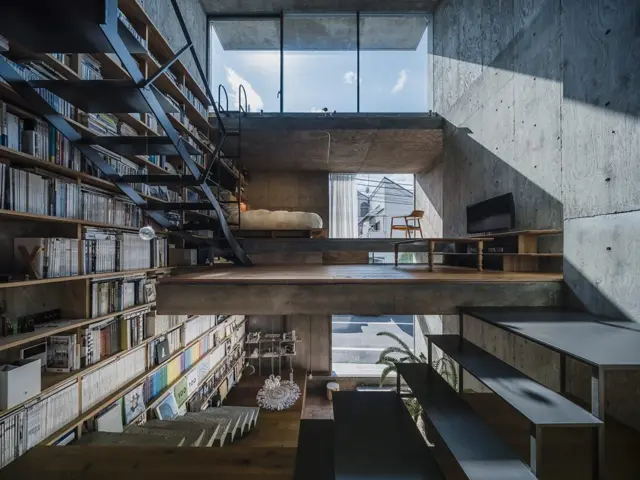 Espacio interior de estilo industrial con biblioteca de doble altura, escaleras metálicas, entrepisos de hormigón y grandes ventanales.