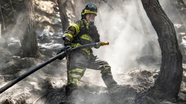 Imagem de um bombeiro combatendo incêndios florestais em um cenário devastado por fumaça e chamas, simbolizando os efeitos das mudanças climáticas observados em 2024, como secas e calor intenso.