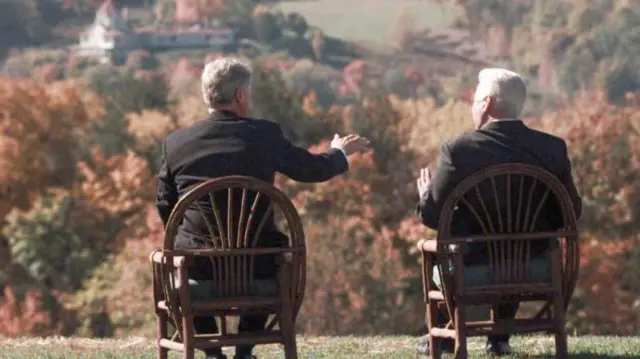 Білл Клінтон та Борис Єльцин сидять на дерев'яних стільцях на пагорбі з видом на природу