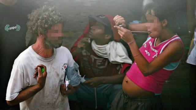 Mulher grávida acendendo cachimbo para fumar crack na Cracolândia