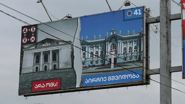 An election billboard above a busy road shows a devastated Ukraine on one side and peaceful Georgia on the other 