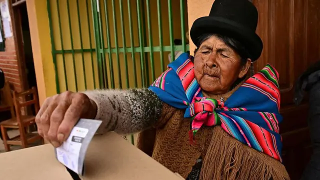 Una mujer boliviana con vestimentas indígenas y un sombrero negro deposita su voto en una urna