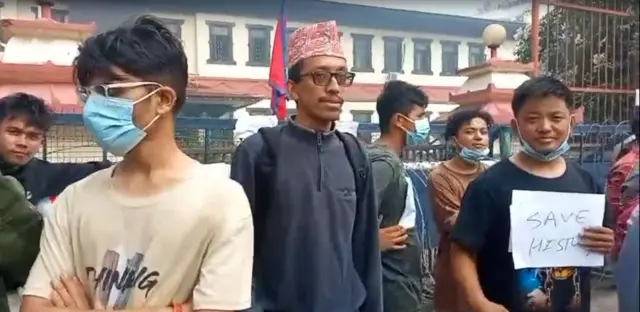 प्रतीक श्रेष्ठ राष्ट्रिय अभिलेखालय बाहिर। नजिकै इतिहास जोगाउ प्लेकार्ड बोेकका अर्का अभियानकर्ता पनि देखिन्छन्