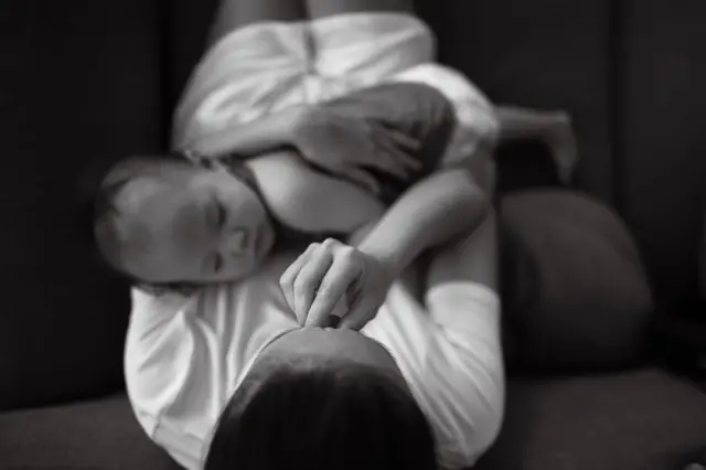 Foto em preto e branco tirada do alto mostra mãe com mãe no rosto segurando bebê