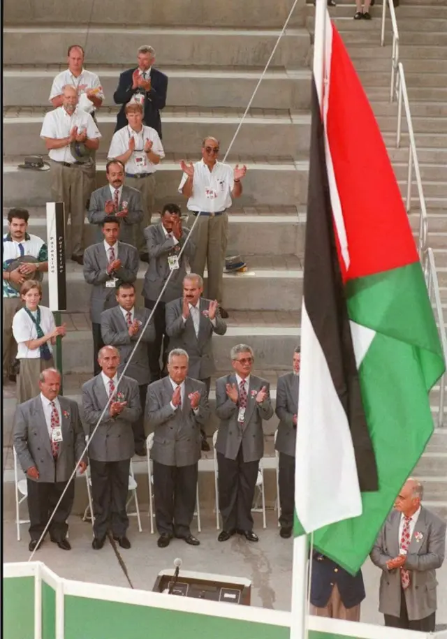 Bandeira palestina sendo hasteada diante da delegação palestina