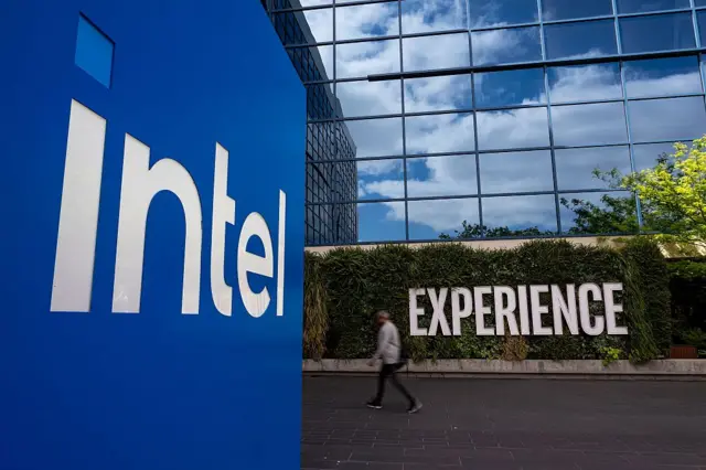 Главный офис Intel в Калифорнии: современное здание с фасадом из стекла, в котором отражаются облака, и белая надпись Intel на синем фоне