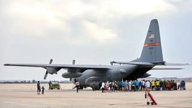 تصویر یک هواپیمای نظامی که شمار زیادی از مهاجران در کنار آن منتظر سوار شدن هستند.