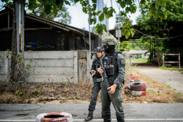 PATTANI, THAILAND - 2023/08/17: Armed troops with assault rifles stand guard at a checkpoint along a rural highway in Pattani.