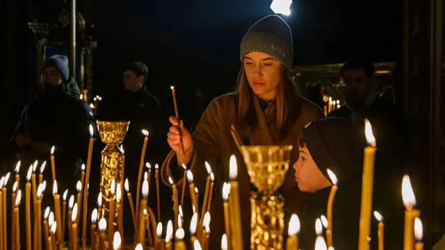 One woman dey light candle wit her son during Christmas Eve service for Kyiv, Ukraine