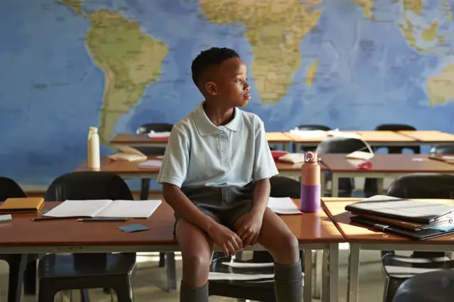 Un écolier, assis sur son bureau dans une salle de classe, détourne le regard