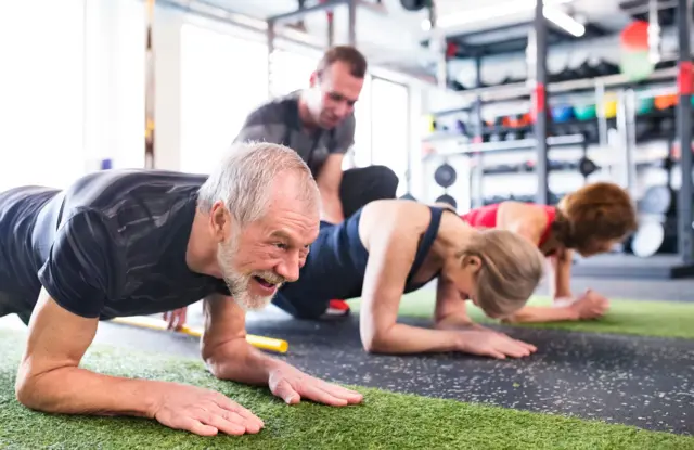 Personas mayores haciendo planchas en gimnasio. 