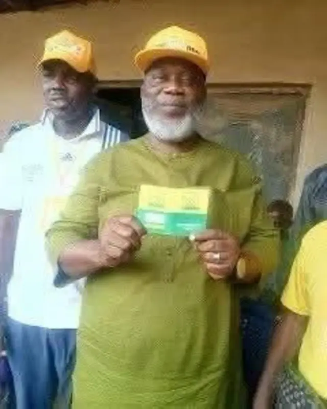 Busari Olakunle tawọn eeyan mọ si Gudugudu wọ asọ toketilẹ alawọ ewe, o fi ọwọ mejeeji mu kaadi idamọ ẹgbẹ oselu accord